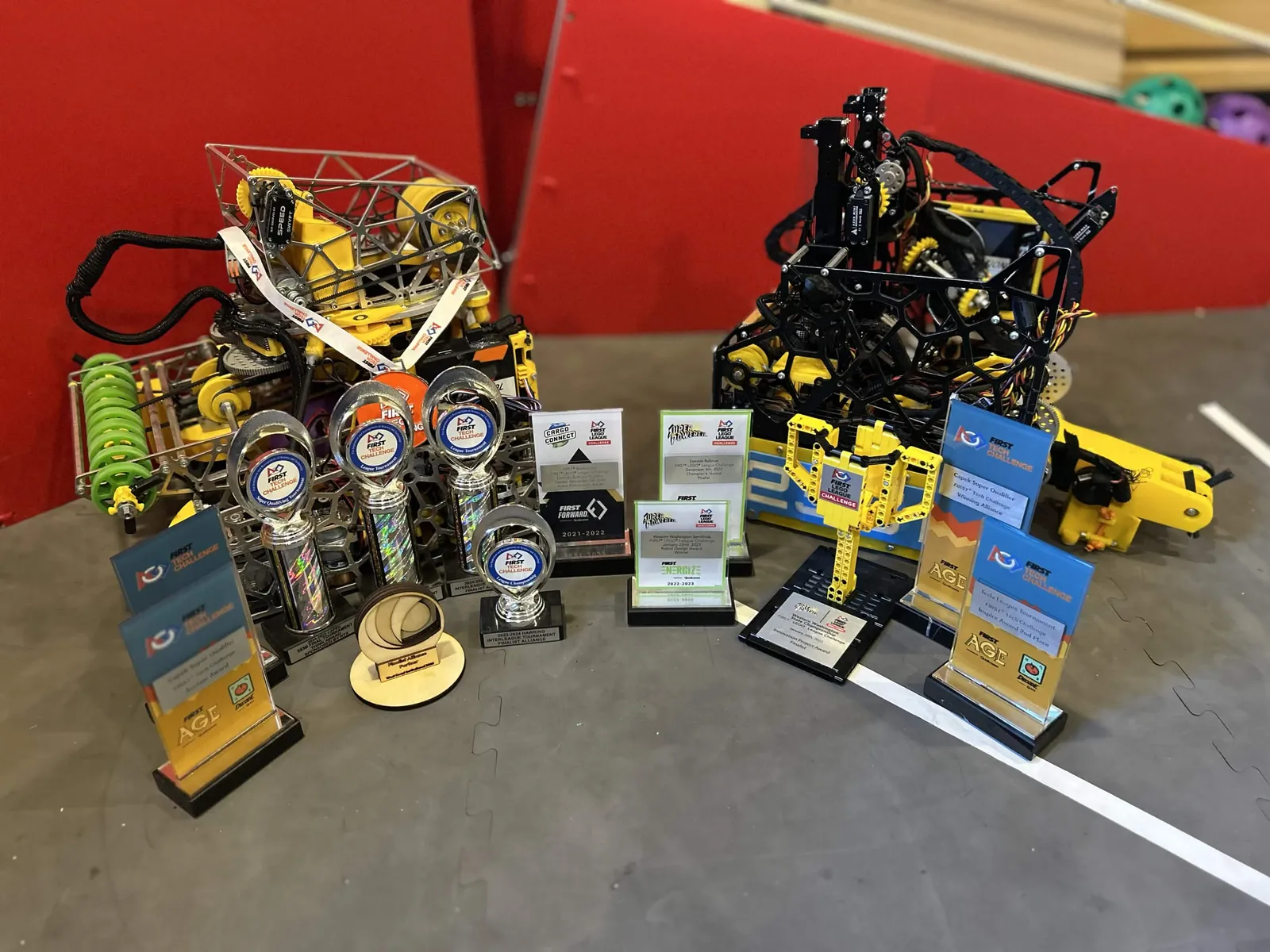 Enigma and Riptide on a field surrounded by the team's award plaques and trophies, from FIRST LEGO League to DECODE