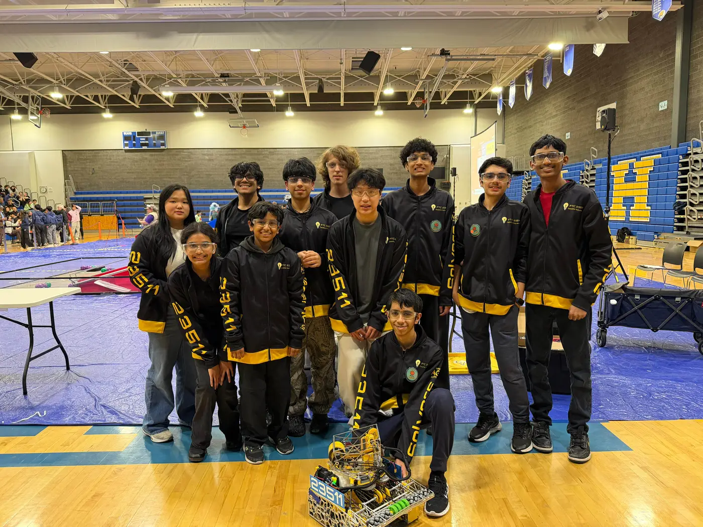 The Seattle Solvers in their black and yellow jackets with Cypher in front of them, in a gym at a competition