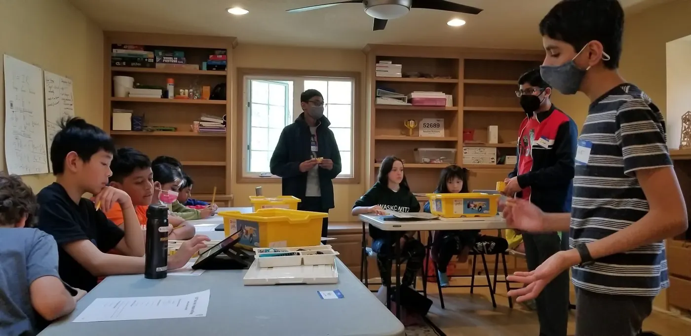 Students at tables with LEGO bins while team members teach at the front of the room