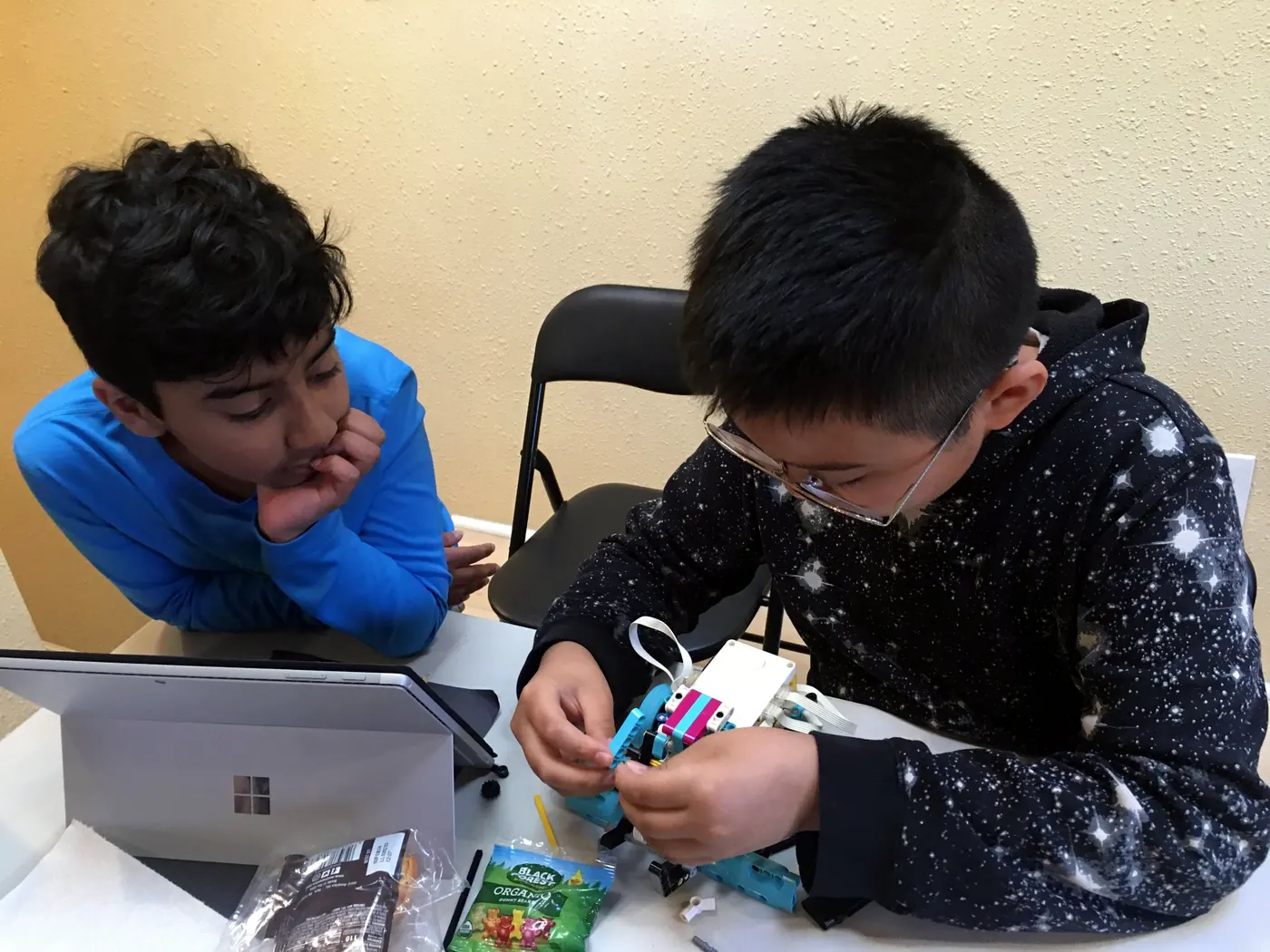 Two students at a class table, one building a LEGO SPIKE robot while the other watches beside a laptop