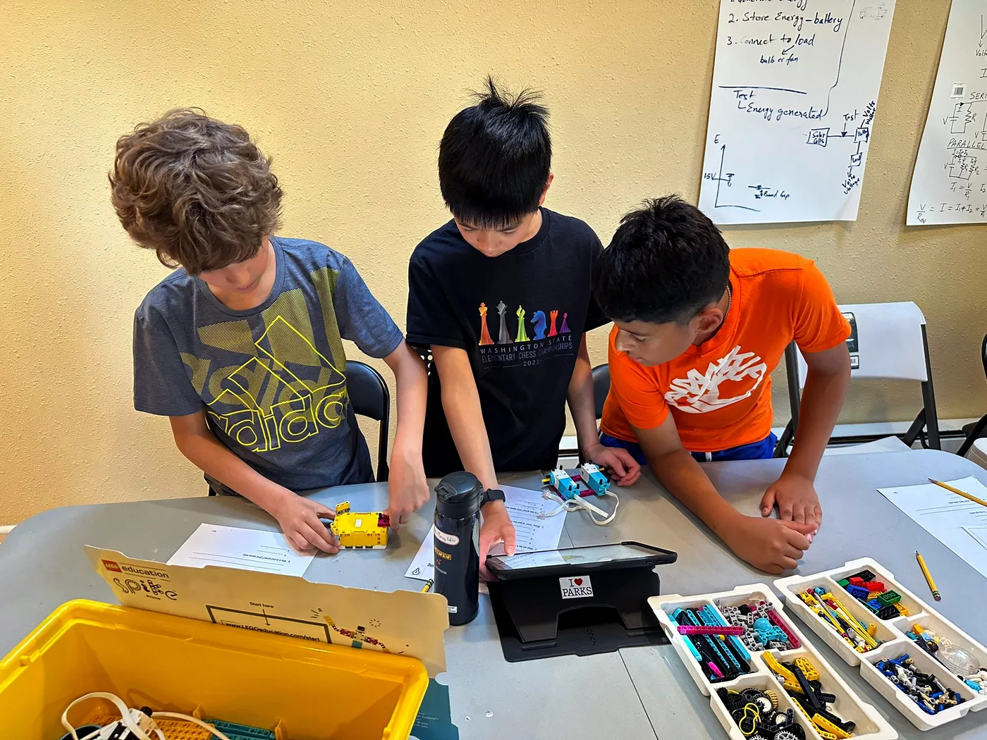 Three kids building a LEGO robot at a class table