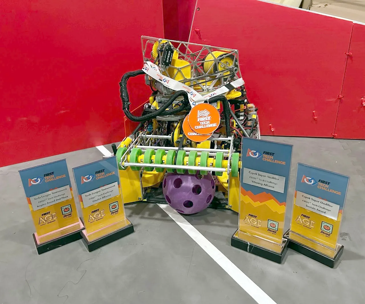 Cypher, our first DECODE robot, on the field behind four award plaques from the Tesla League Tournament and the Capek Super Qualifier
