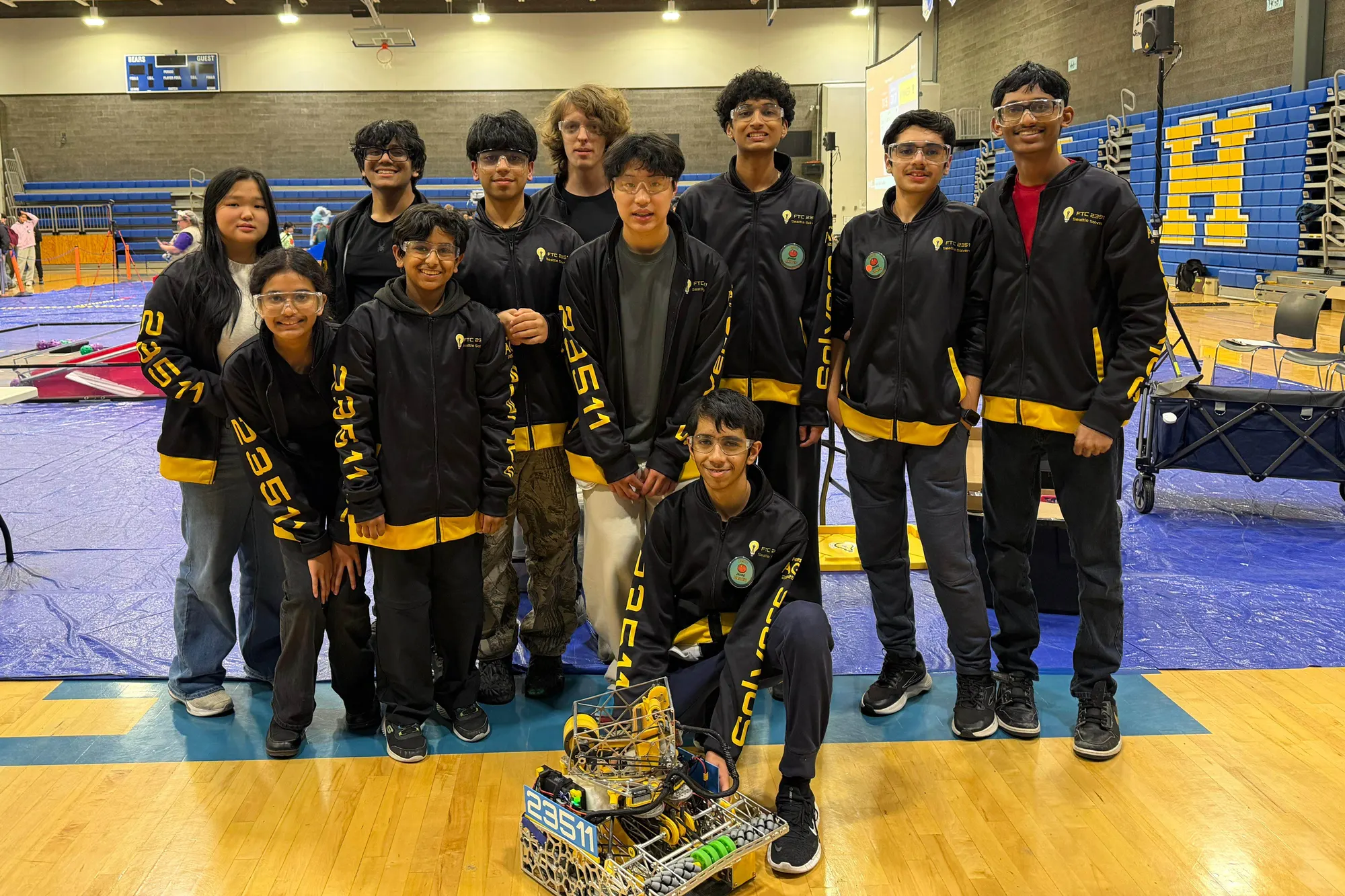 The Seattle Solvers in team jackets with their robot in a school gym at a competition
