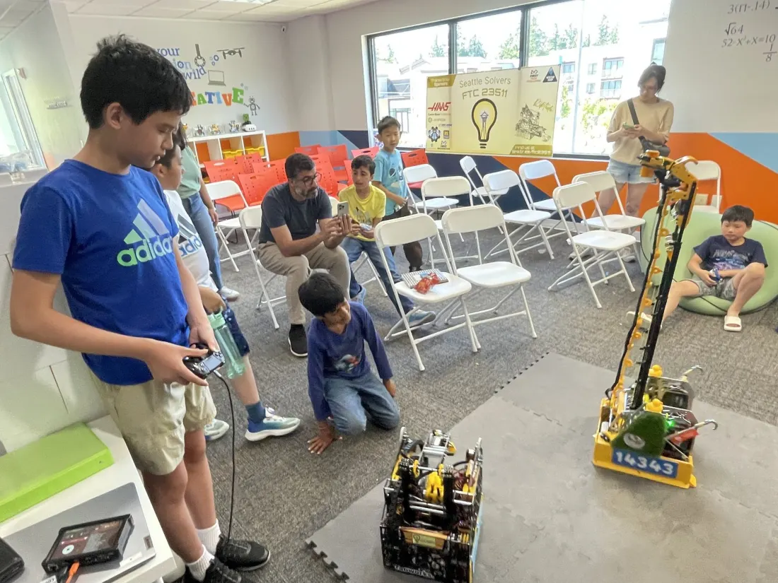 A boy drives the robot with a controller while other kids watch at CodeWiz