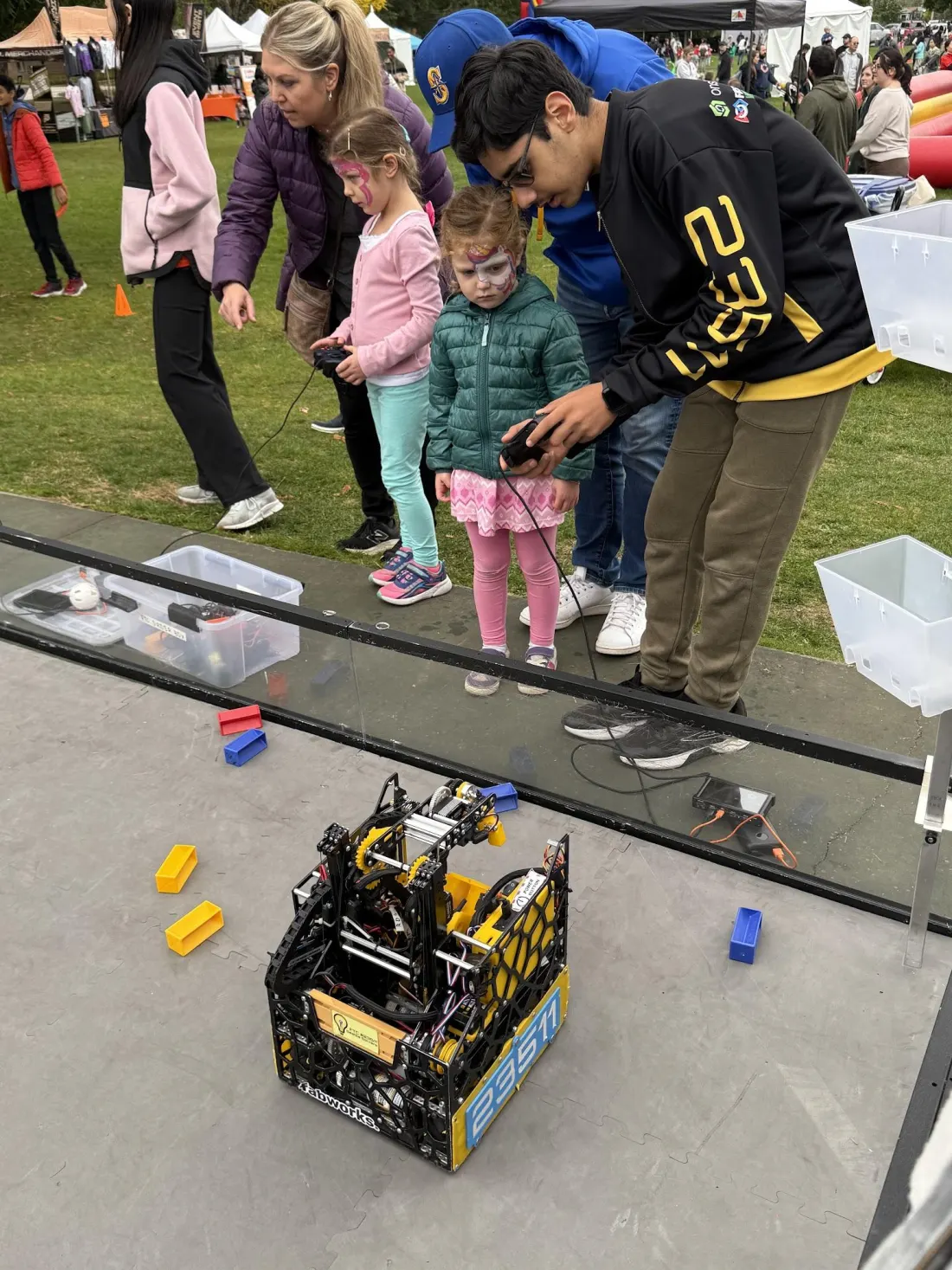 A team member helps a young girl drive the robot on an outdoor demo field at Salmon Days