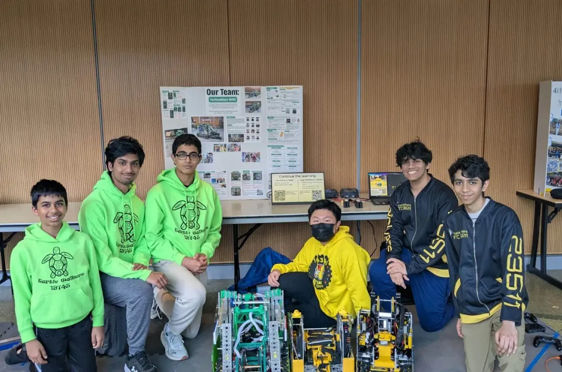 Seattle Solvers members with students in green team hoodies, gathered behind three robots at the STEM Kit Expo