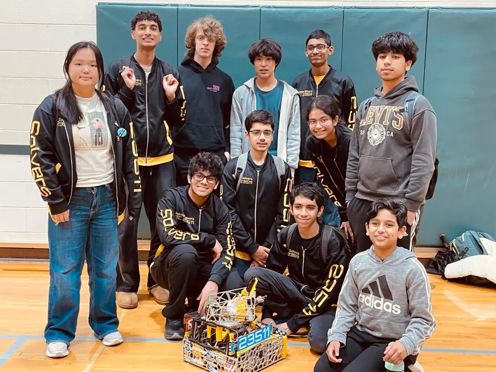 The Seattle Solvers in their black and yellow jackets around Cypher, in a gym with green padding on the wall