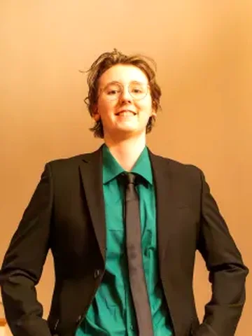 Kai in a black suit, green shirt and dark tie